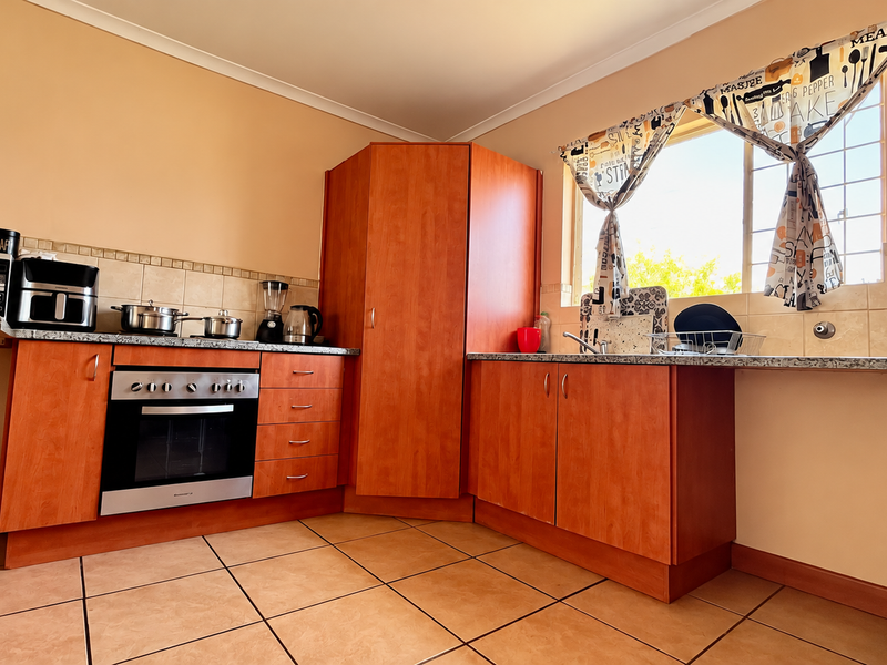A functional kitchen featuring wooden cabinetry, granite countertops, a built-in oven, and tiled flooring, offering a practical layout with ample storage space.
