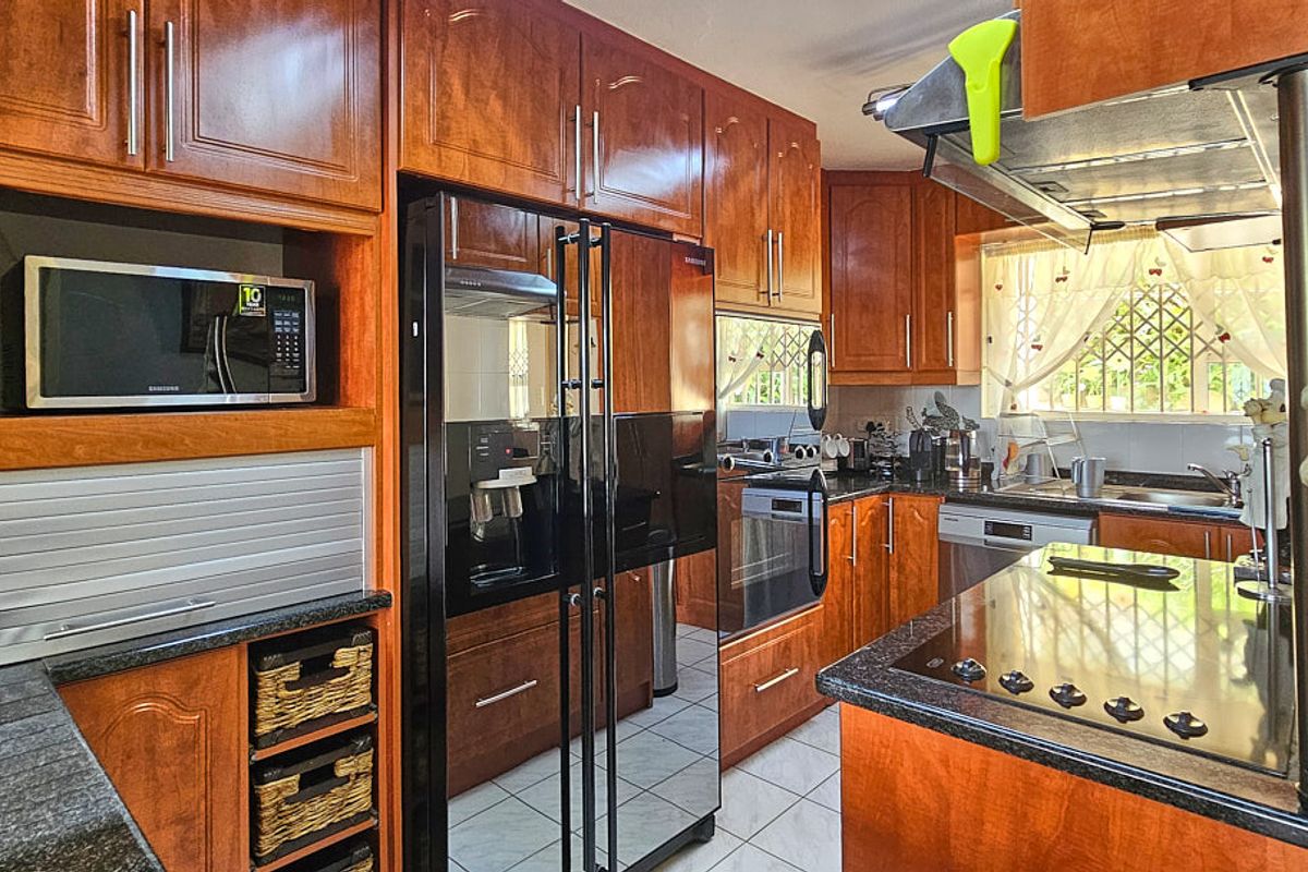 A well-equipped kitchen featuring warm-toned wooden cabinetry, granite countertops, built-in appliances, and tiled flooring with security bars on the windows.