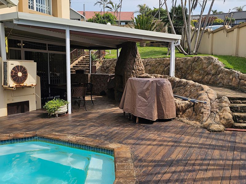 Outdoor entertainment area featuring a swimming pool, covered patio with built-in braai, and tiered garden access via stone-look retaining walls and stairs.