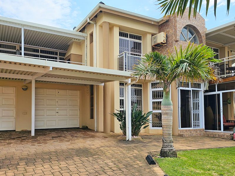 Front elevation of a multi-story house featuring a double garage, paved driveway, covered patio area, and balcony with security gates.