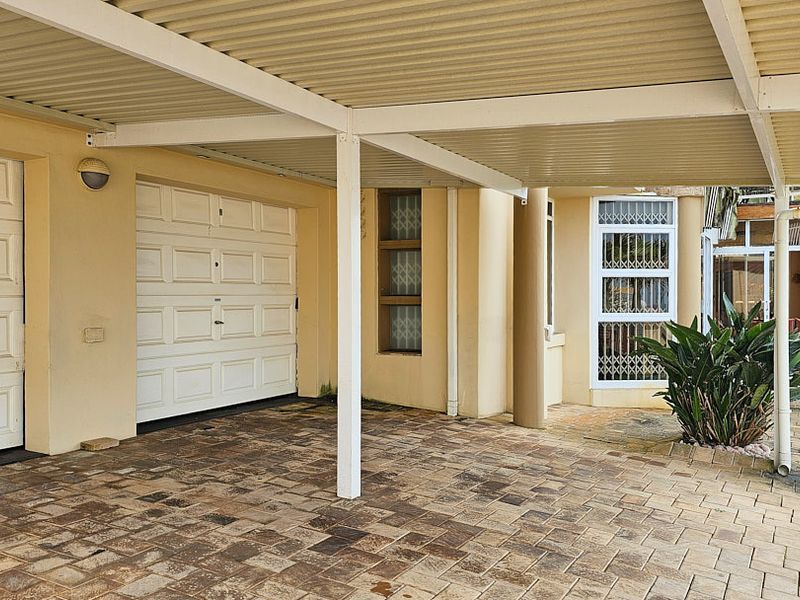 A covered carport area featuring paved flooring, dual garage access, and security-fitted windows, providing sheltered parking space for the property.