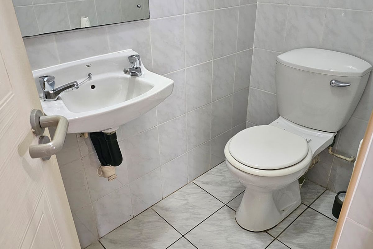 A compact bathroom featuring a wall-mounted washbasin, a standard toilet, and neutral ceramic tiling throughout.