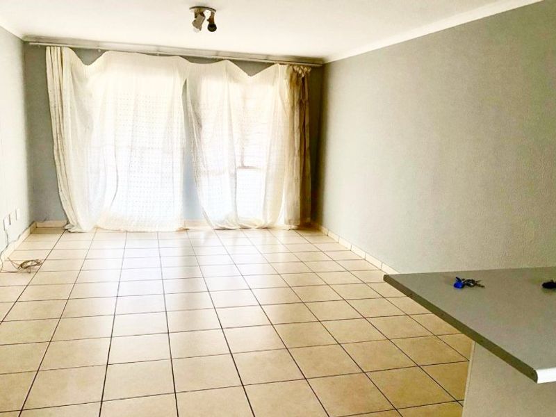 An empty open-plan living area featuring neutral tiled flooring, a breakfast bar, and large windows with curtain tracks.