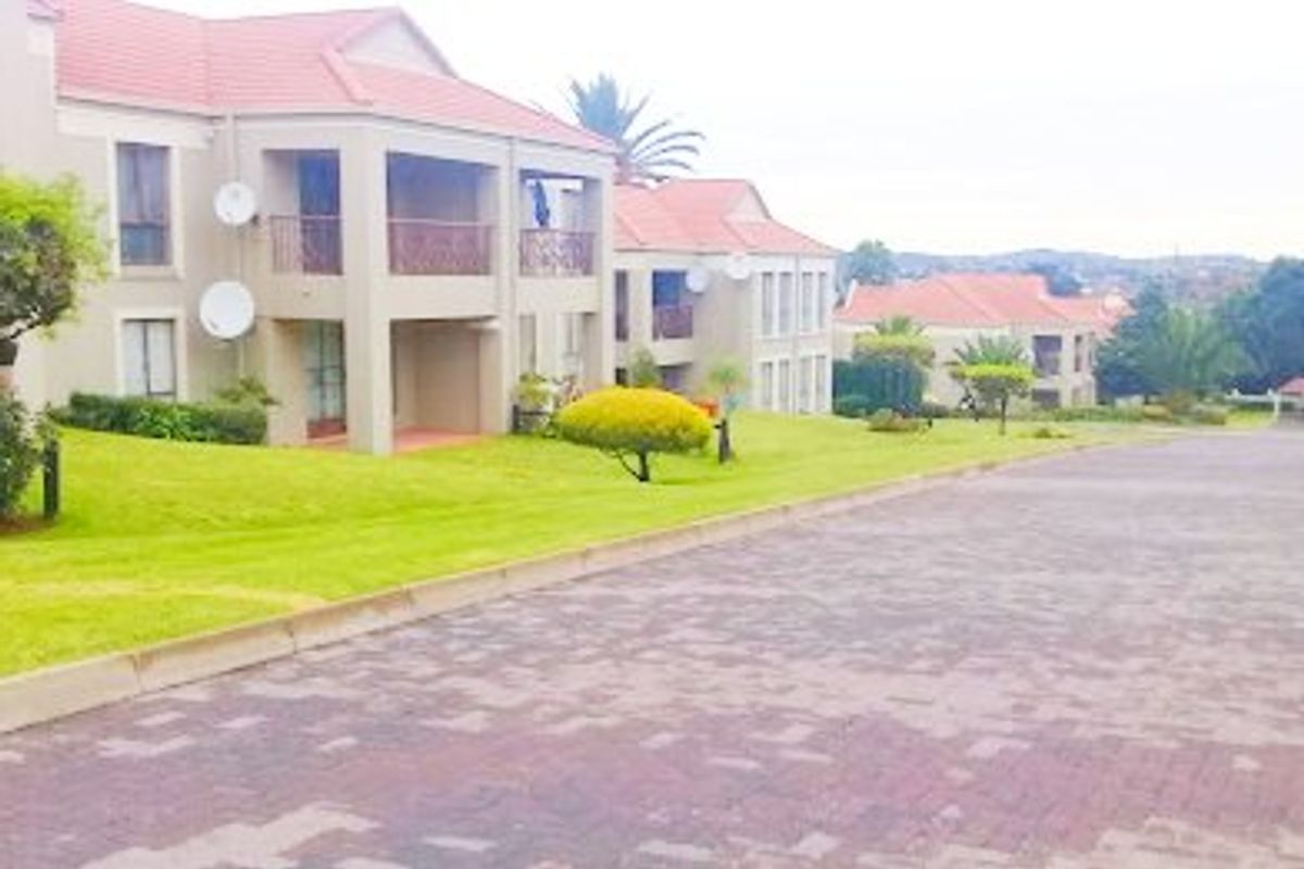 A view of the apartment complex exterior featuring tiled roofs, balconies, and a paved driveway set within a landscaped garden area.