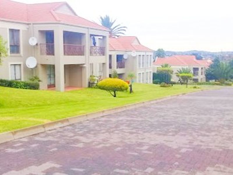 A view of the apartment complex exterior featuring tiled roofs, balconies, and a paved driveway set within a landscaped garden area.