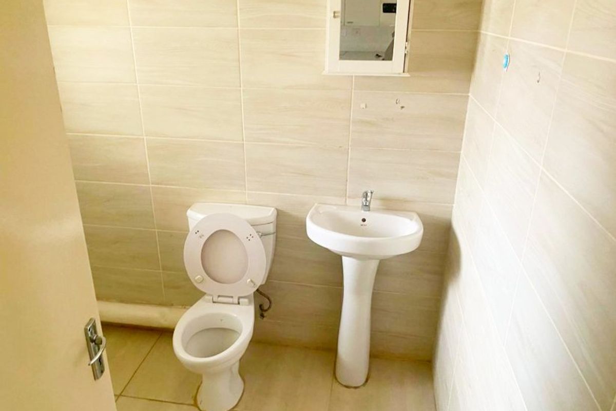 A functional bathroom featuring a pedestal washbasin, toilet, and wall-mounted medicine cabinet with neutral ceramic tiling throughout.