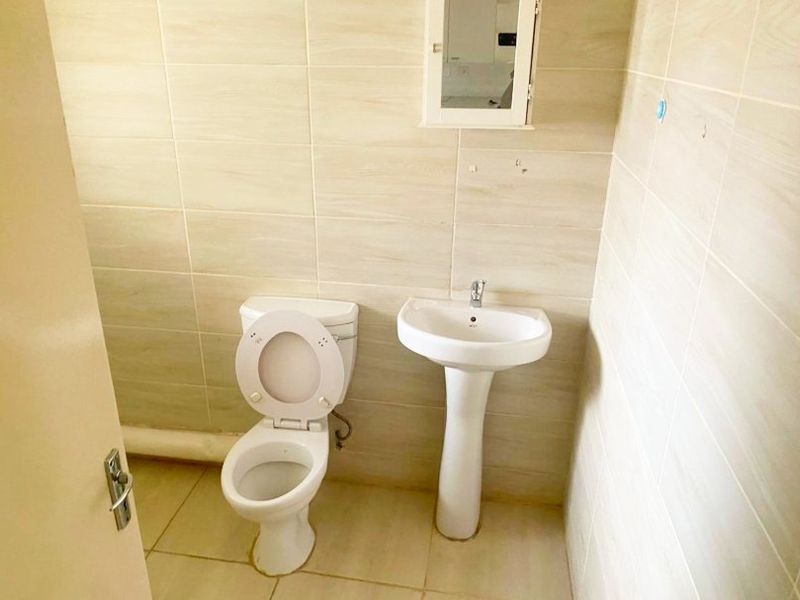 A functional bathroom featuring a pedestal washbasin, toilet, and wall-mounted medicine cabinet with neutral ceramic tiling throughout.