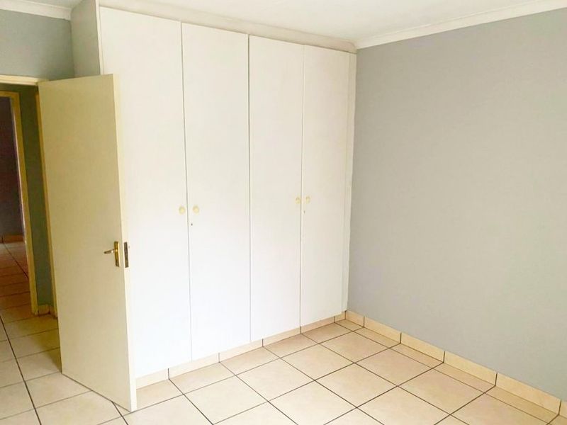 A clean, empty bedroom featuring neutral wall paint, tiled flooring, and ample built-in cupboard storage space.