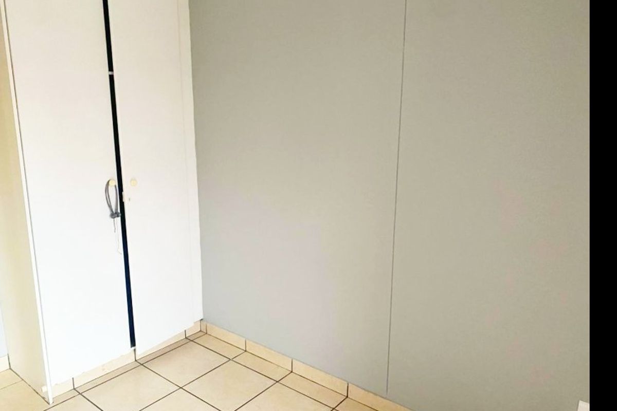 A simple, empty bedroom featuring neutral wall finishes, tiled flooring, and a built-in wardrobe.
