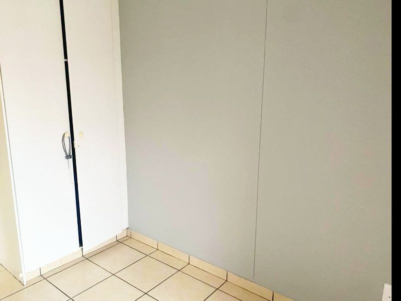 A simple, empty bedroom featuring neutral wall finishes, tiled flooring, and a built-in wardrobe.
