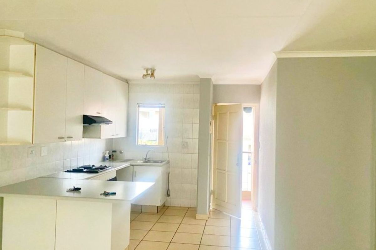 A functional kitchen featuring white built-in cabinetry, laminate countertops, a gas hob with extractor, and tiled flooring, leading directly to an exterior doorway.