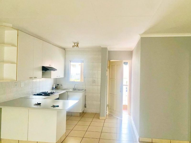 A functional kitchen featuring white built-in cabinetry, laminate countertops, a gas hob with extractor, and tiled flooring, leading directly to an exterior doorway.