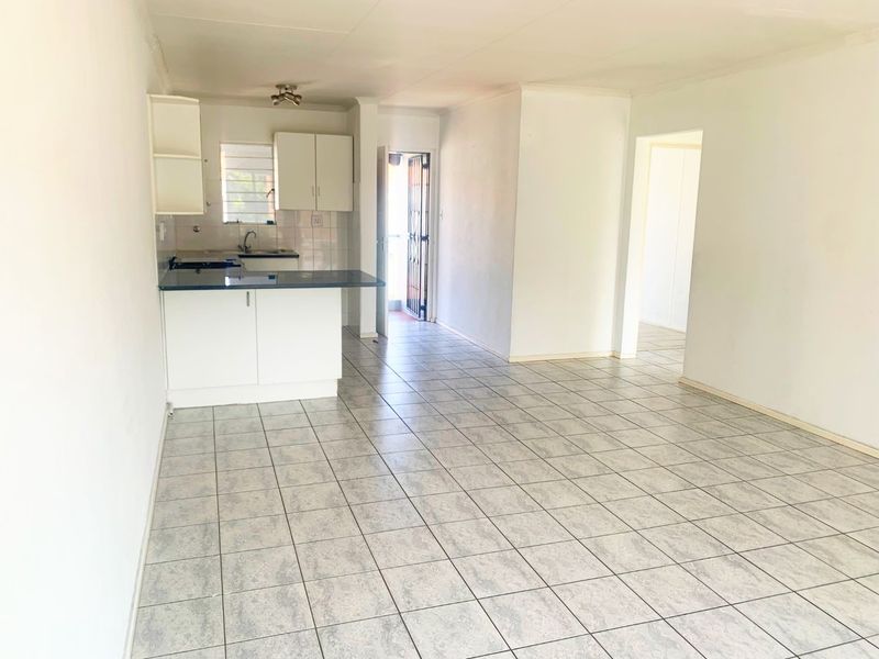 An open-plan living and kitchen area featuring tiled flooring, basic cabinetry, and direct access to an exterior security gate.