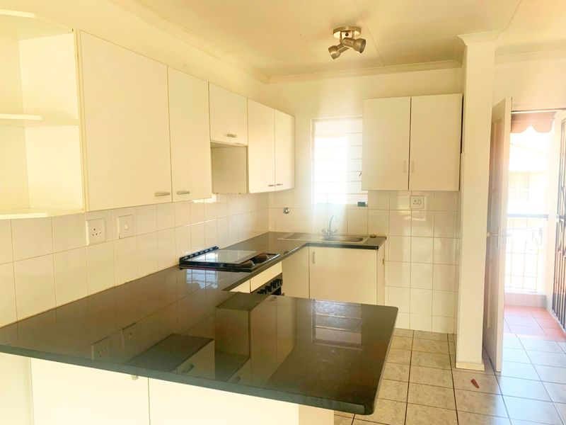 A functional kitchen featuring white built-in cabinetry, dark countertops, a built-in hob and oven, and tiled finishes, offering a clean and practical workspace.
