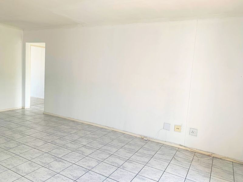 An empty living area featuring neutral ceramic floor tiles and plain white walls, providing a blank canvas for interior design.