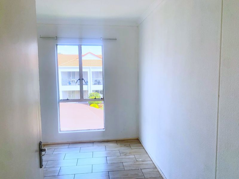 A bright, empty bedroom featuring modern wood-look tiled flooring and a large window with an aluminium frame.