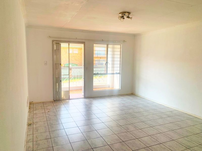 An empty living room featuring tiled flooring, a ceiling light fixture, and a sliding glass door providing access to an outdoor balcony area.