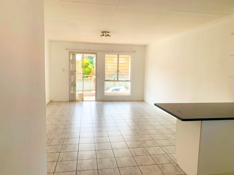 An open-plan living area featuring tiled flooring, a breakfast bar, and access to an outdoor space through a sliding glass door.