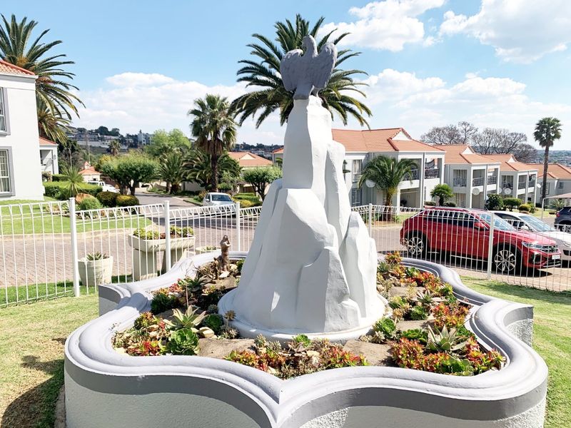A well-maintained communal garden area featuring a decorative central fountain with an eagle sculpture, surrounded by landscaped succulents and secure perimeter fencing.