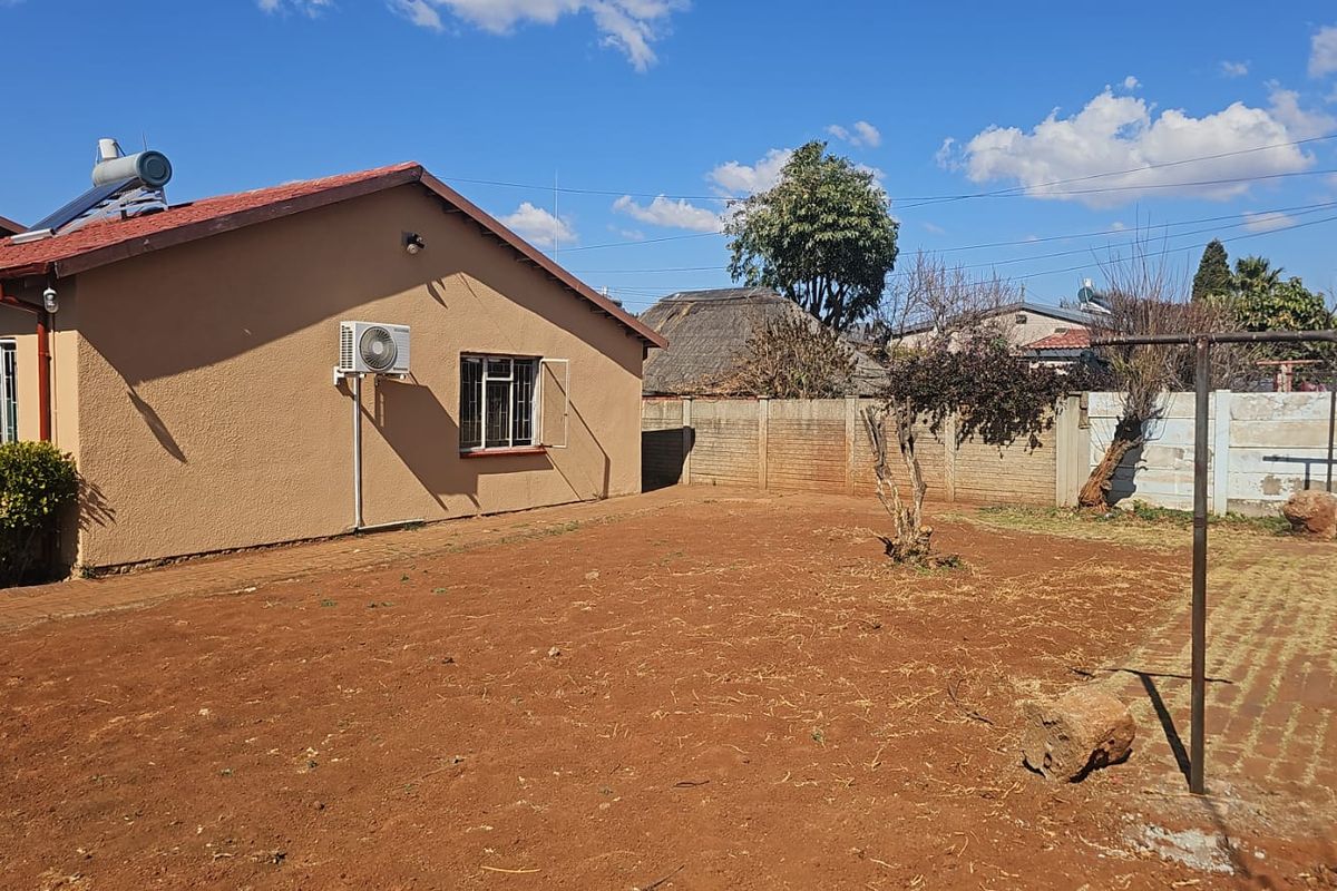 Rear view of the property featuring a large open garden area, precast boundary wall, and exterior mounted air conditioning unit.