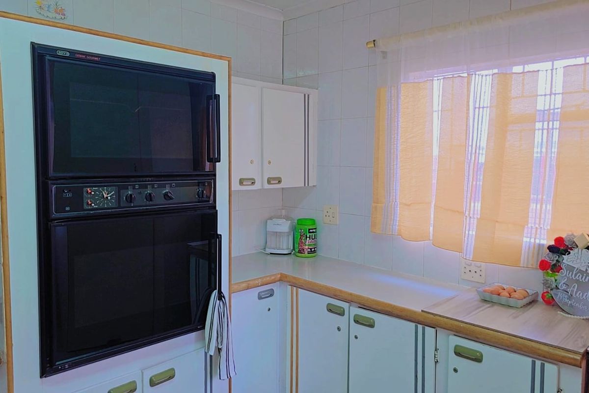 A functional kitchen featuring built-in double ovens, white cabinetry, and tiled wall finishes, offering a practical layout with potential for modern updates.