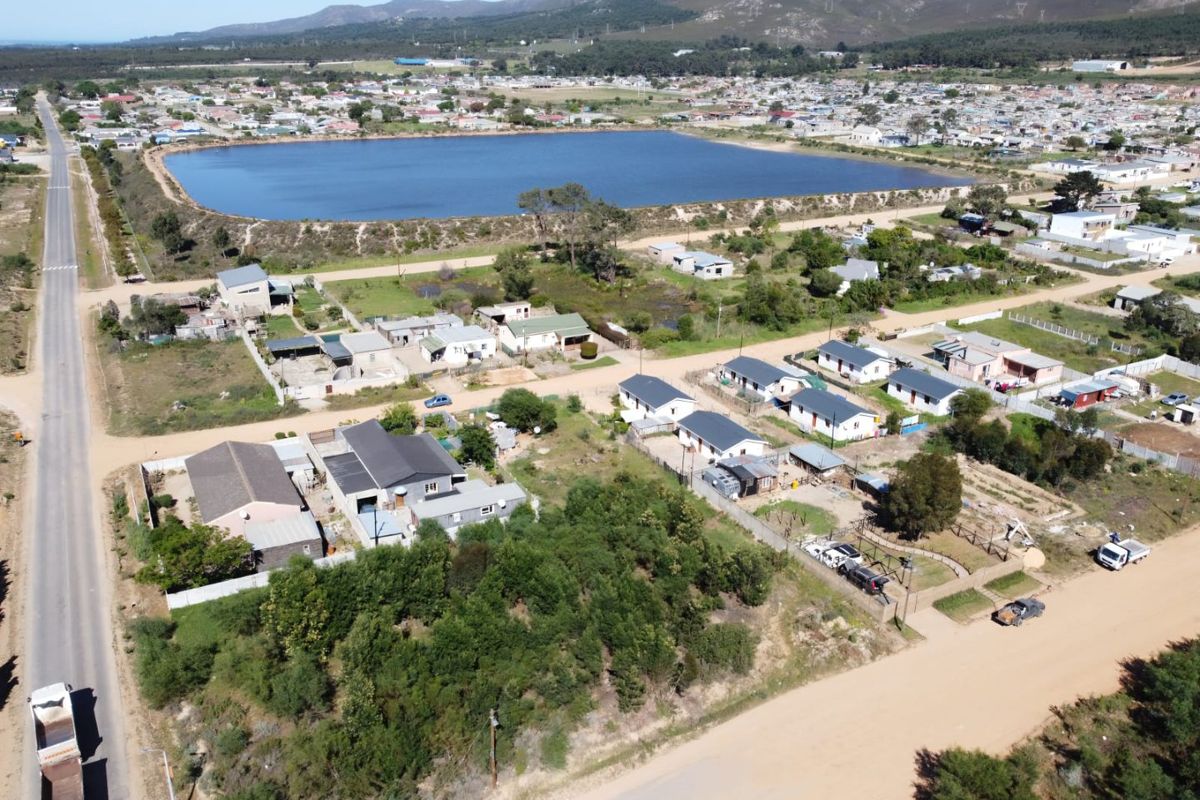 Aerial view of a residential area featuring vacant land plots, unpaved access roads, and proximity to a large reservoir and mountain landscape.