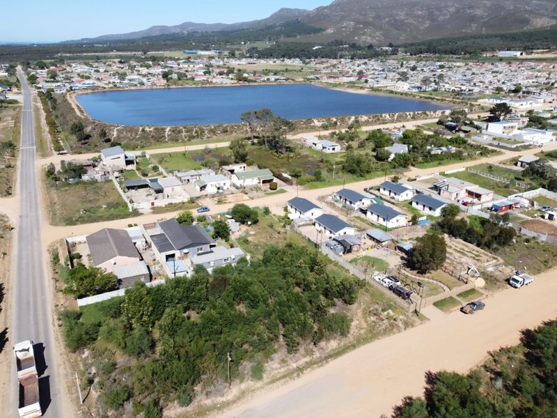 Aerial view of a residential area featuring vacant land plots, unpaved access roads, and proximity to a large reservoir and mountain landscape.