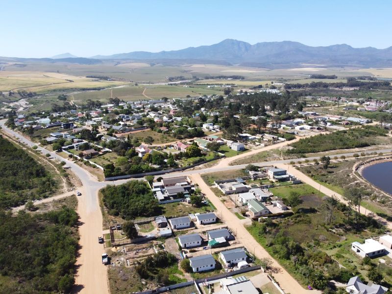 An aerial view of a residential neighborhood featuring unpaved roads, surrounding landscape, and a distant mountain range.