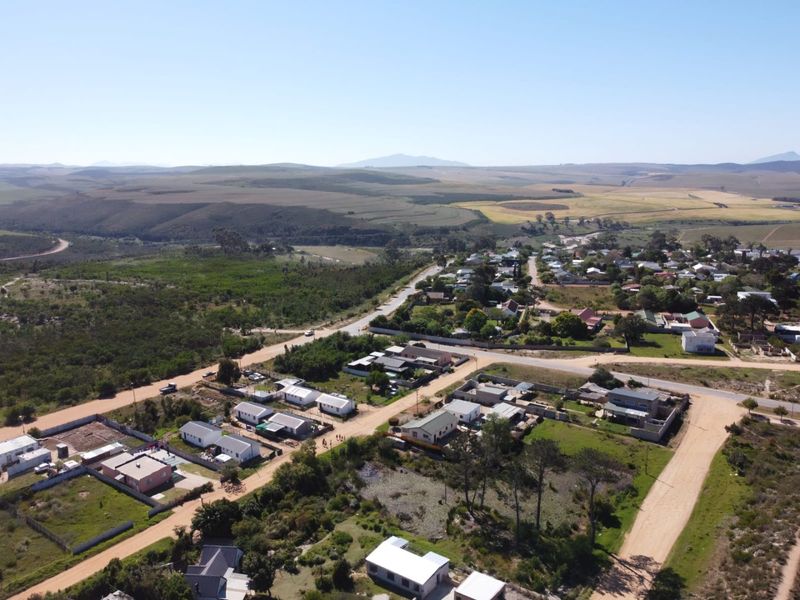 Aerial view of a residential area featuring vacant land plots, established homes, and surrounding rural landscape with unpaved road access.