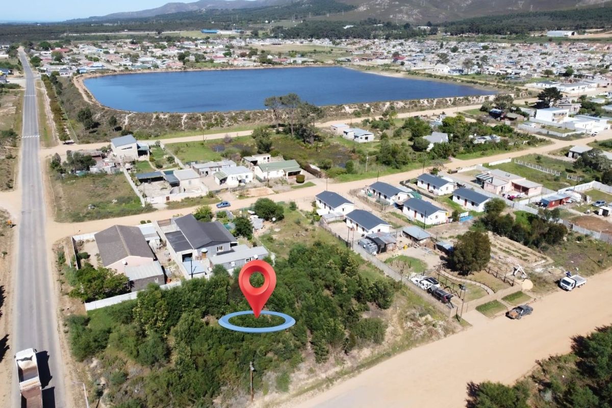 Aerial view of a vacant residential plot situated in a developing neighborhood with nearby water reservoir and mountain views.