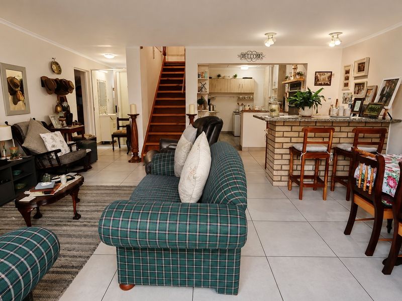 Open-plan living and dining area featuring a brick breakfast bar, tiled flooring, and a wooden staircase leading to the upper level.