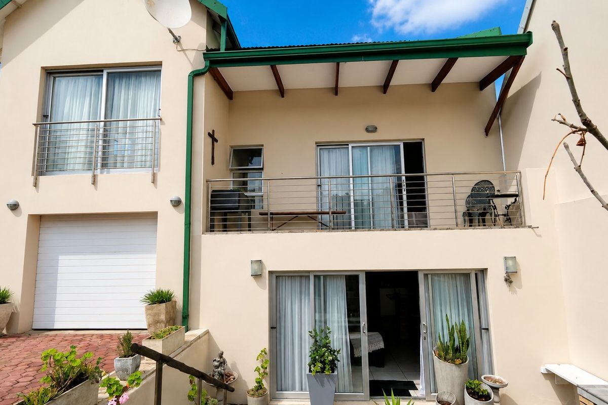 Rear elevation of the property featuring a balcony with stainless steel balustrades, sliding glass doors, and a ground-level garage entrance.