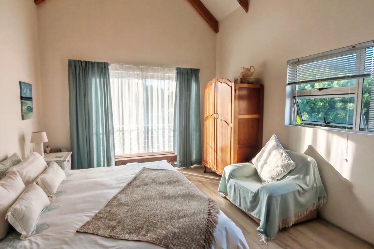 A bright bedroom featuring a high vaulted ceiling with exposed timber beams, laminate flooring, and large windows with natural light.