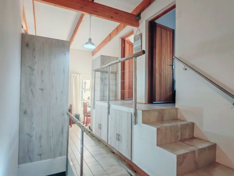 A bright hallway featuring exposed timber ceiling beams, built-in storage cabinetry, and a tiled staircase with a modern stainless steel handrail.
