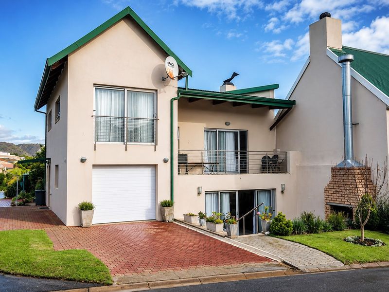 A well-maintained two-story residential property featuring a paved driveway, integrated garage, balcony, and an external brick fireplace.