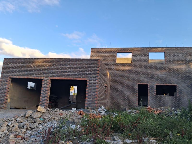 A partially constructed double-story house featuring a face brick facade and an open double garage structure, currently in the early stages of development.