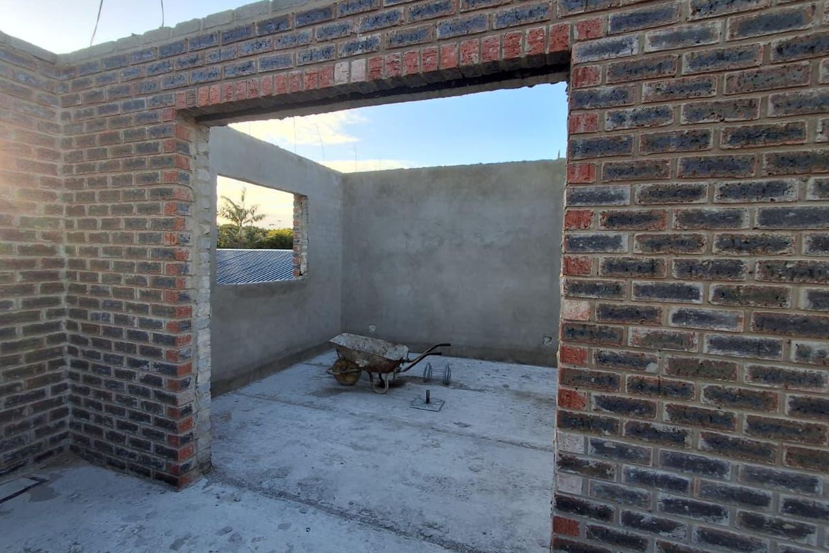 An unfinished room under construction featuring exposed brick walls and a concrete floor slab, currently lacking roofing, windows, and doors.