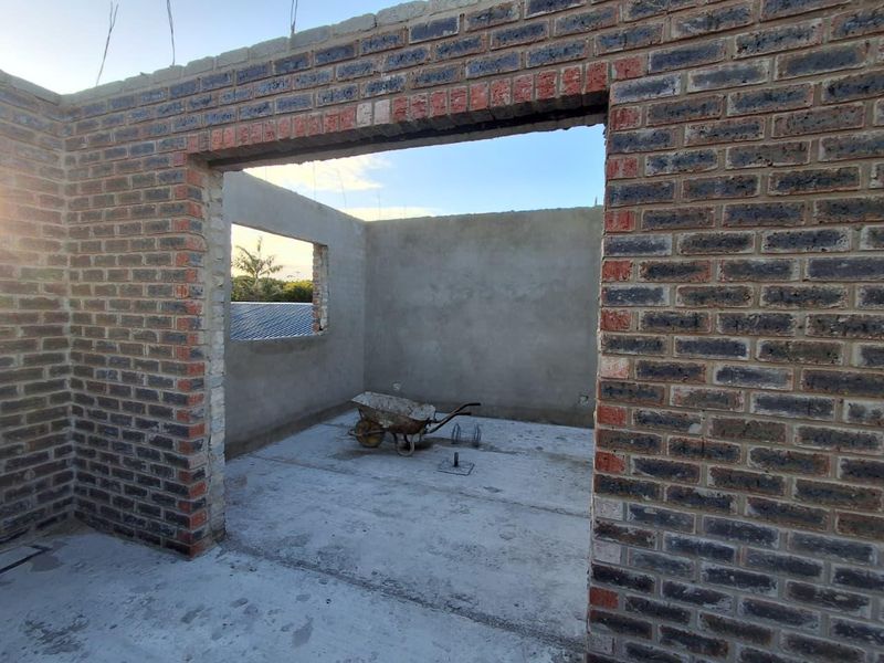 An unfinished room under construction featuring exposed brick walls and a concrete floor slab, currently lacking roofing, windows, and doors.