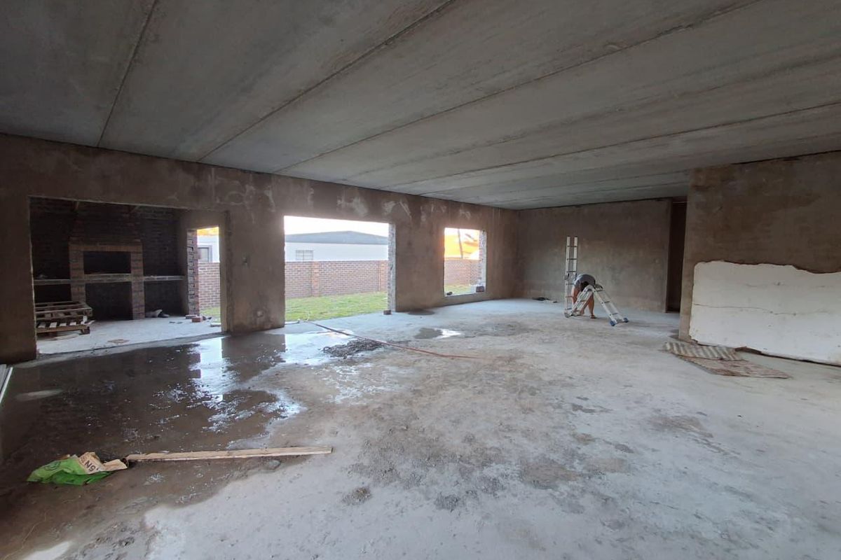 An expansive open-plan living area currently under construction, featuring raw concrete surfaces and a built-in brick fireplace, awaiting final finishes and flooring.