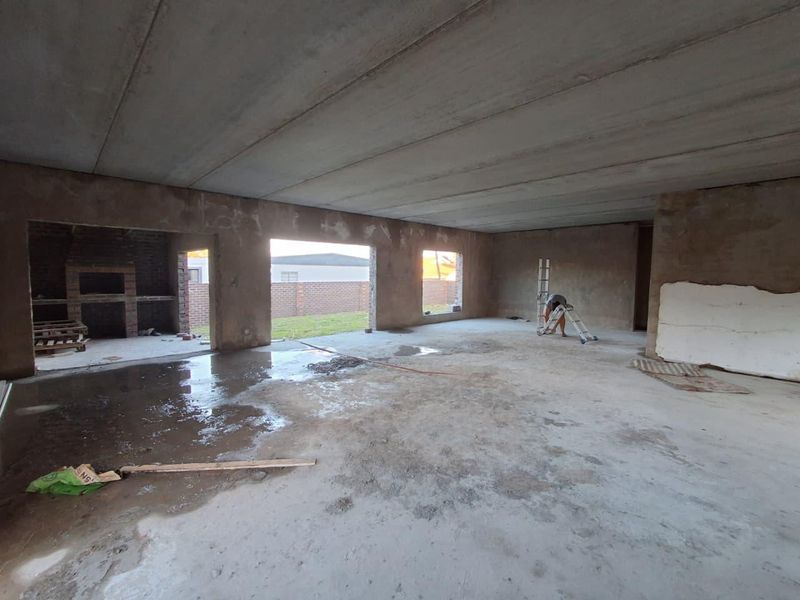 An expansive open-plan living area currently under construction, featuring raw concrete surfaces and a built-in brick fireplace, awaiting final finishes and flooring.