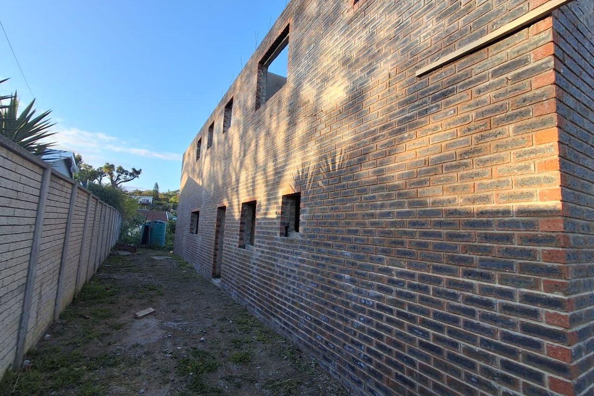 Exterior view of a property under construction, featuring exposed face brick walls and open window frames along the side elevation.