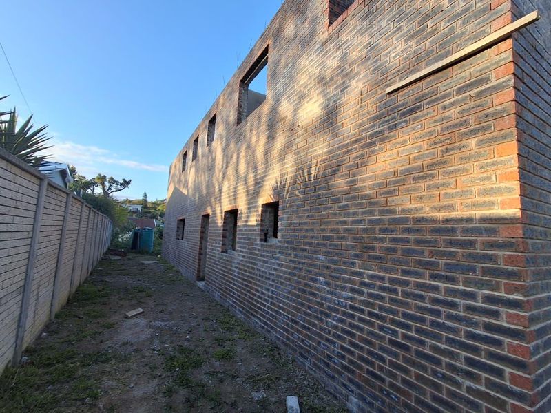 Exterior view of a property under construction, featuring exposed face brick walls and open window frames along the side elevation.