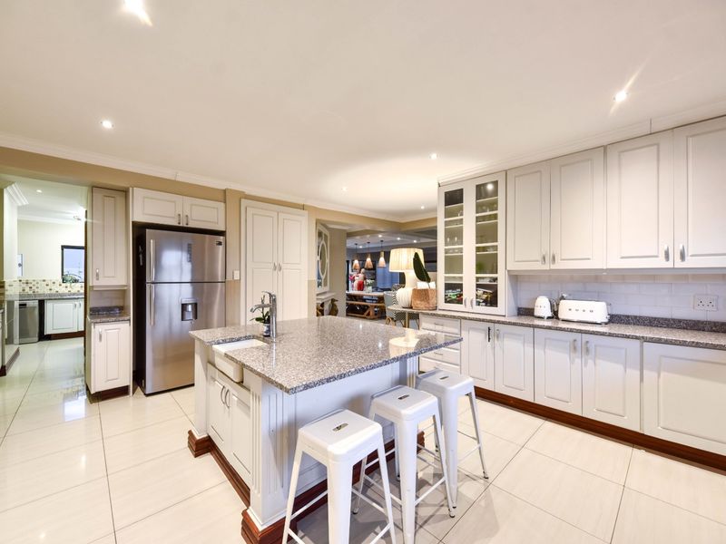 Spacious open-plan kitchen featuring a central island with a farmhouse sink, granite countertops, ample cabinetry, and modern tiled flooring.