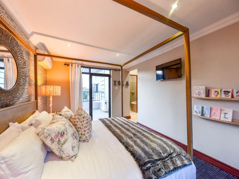 A well-maintained bedroom featuring a four-poster bed frame, recessed lighting, air conditioning, and direct access to a private balcony and en-suite bathroom.