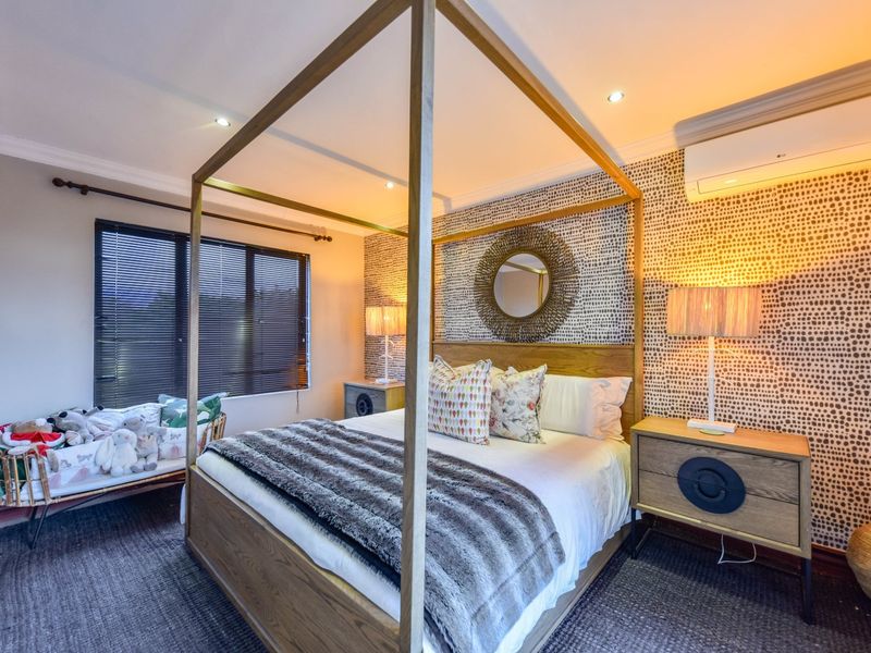 A well-maintained bedroom featuring a four-poster bed, patterned accent wall, split-system air conditioning, and recessed downlighting.