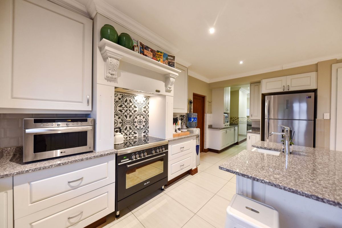 A well-appointed kitchen featuring white shaker cabinetry, granite countertops, a central island, and a decorative tiled backsplash with a built-in oven and extractor.
