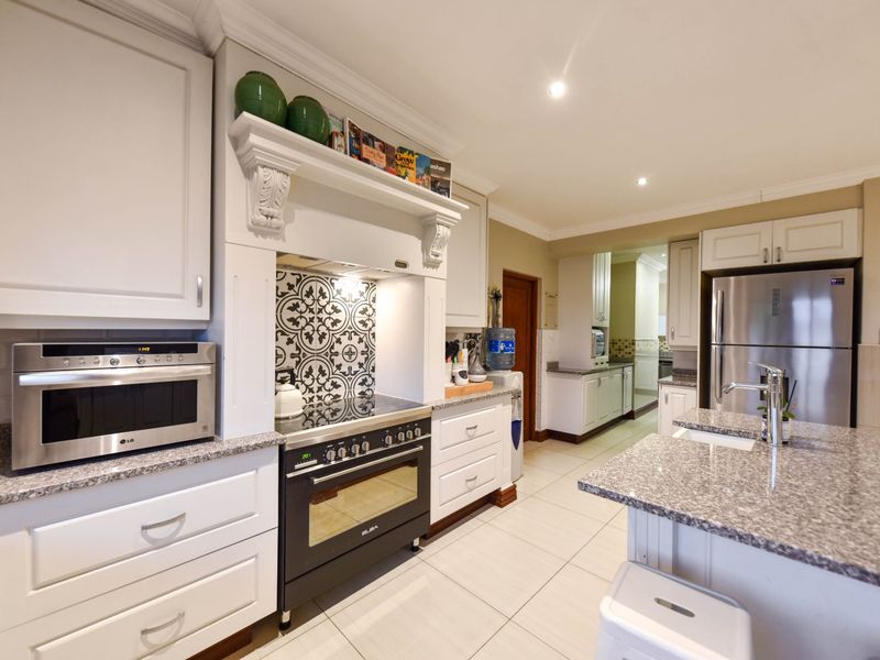 A well-appointed kitchen featuring white shaker cabinetry, granite countertops, a central island, and a decorative tiled backsplash with a built-in oven and extractor.