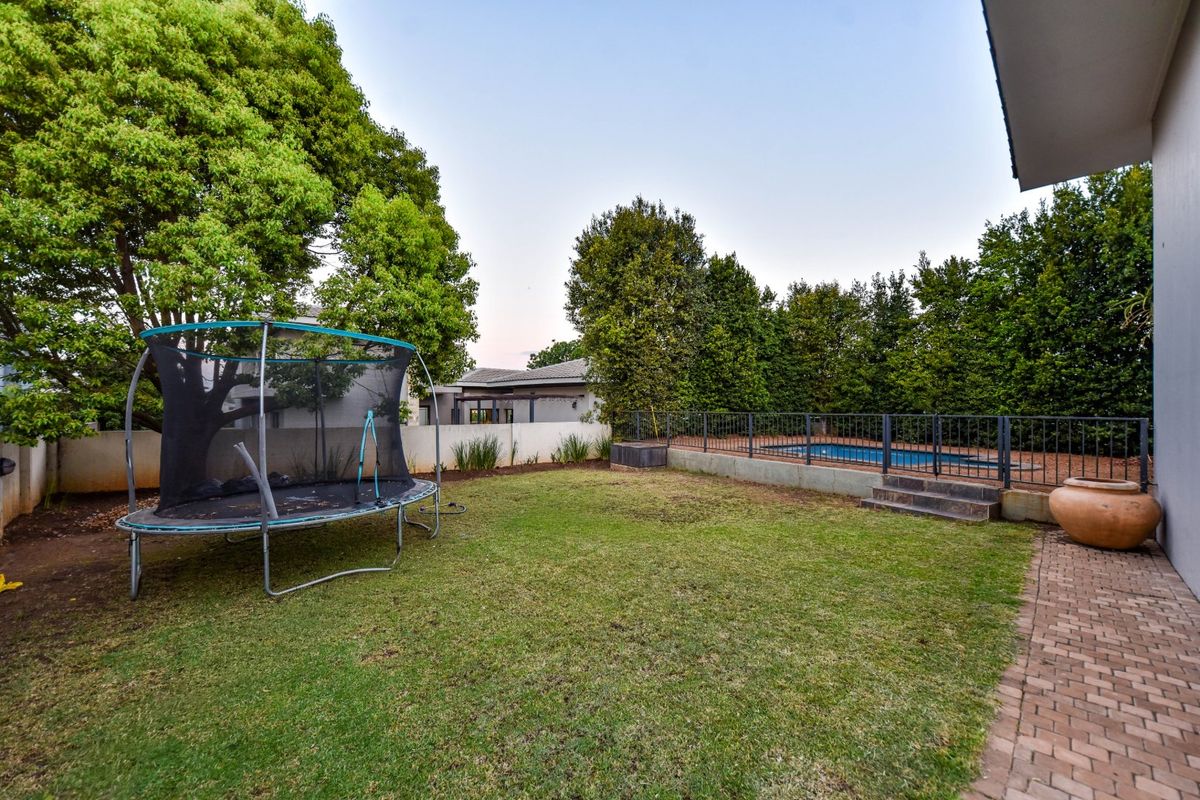 A spacious rear garden featuring a well-maintained lawn, a paved patio area, and a fenced swimming pool with a retaining wall.