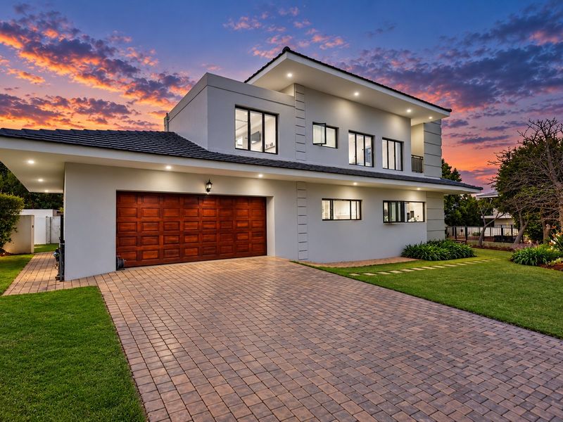A modern two-story residential property featuring a paved driveway, double garage, and well-maintained landscaping, captured during a vibrant sunset.