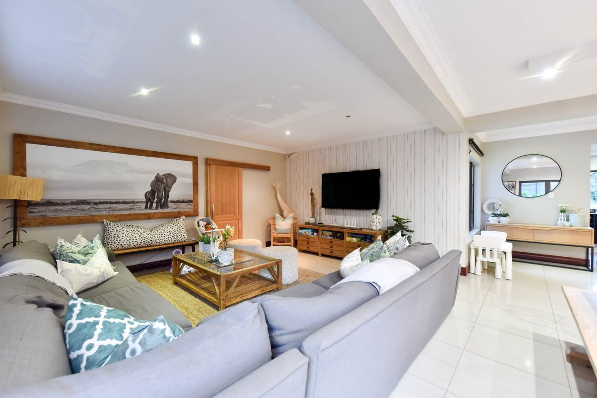 Spacious living room featuring tiled flooring, recessed downlighting, and a feature wall, offering a comfortable and well-lit area for relaxation.